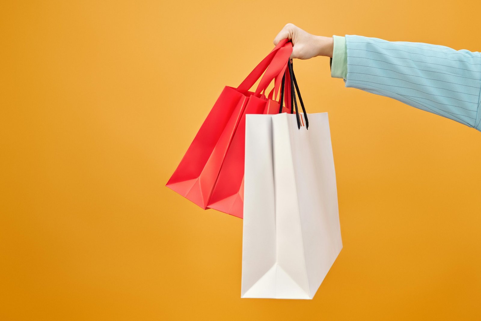 About Us A hand holds colorful shopping bags against a bright yellow backdrop, highlighting retail shopping.