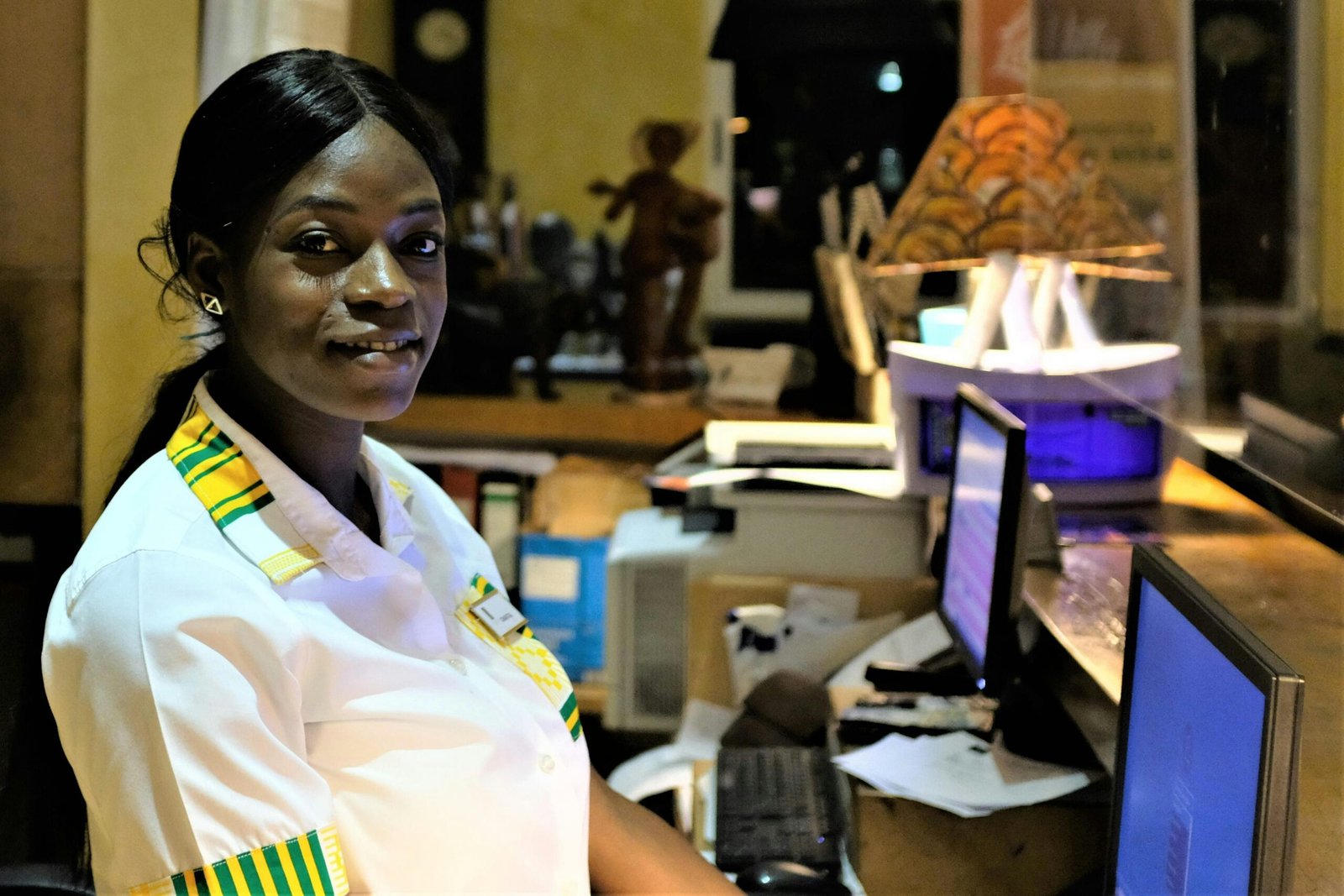 About Us Friendly woman in uniform at hotel reception desk, Accra, Ghana.